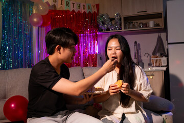 A man and woman are eating food together in a living room