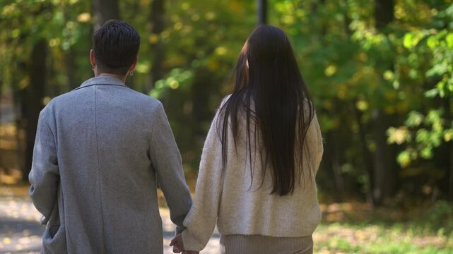 In a picturesque autumn park, a couple romantically holds hands, surrounded by vibrant falling leaves