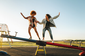 High school friends balancing on a seesaw in a sunny park, enjoying a fun moment together
