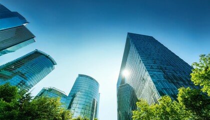 Fototapeta premium A vibrant view of modern skyscrapers reflecting sunlight against a clear blue sky, framed by greenery below.