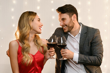 Romantic young couple with glasses of red wine on date in restaurant, celebrating Valentine's Day or anniversary together.