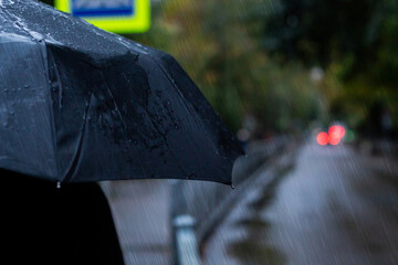 Portrait of a person holding black umbrella outside during the rain. Raindrops and light from city and cars. Rainy weather and forecast concept. Photo taken in Kaliningrad city, Russia © Krievietka