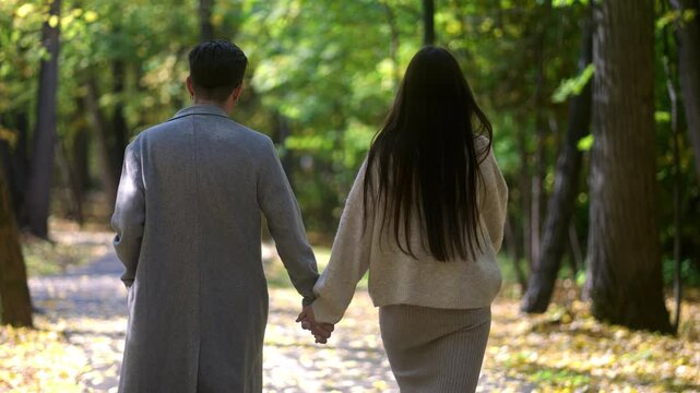 A couple strolls hand in hand through a peaceful forest, surrounded by lush trees and colorful autumn leaves