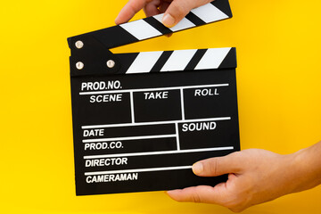 Male hand closing black wooden movie clapperboard on a yellow background, concept of film production and entertainment