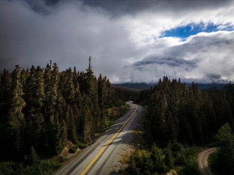 Aerial view of winding road through dense forest under dramatic sky with clouds, Agassiz, Canada.