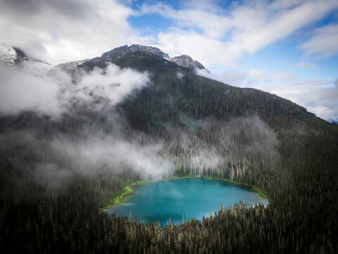 Aerial view of serene forest and tranquil lake surrounded by breathtaking mountains and misty clouds, Agassiz, Canada.