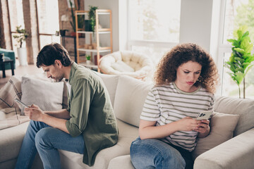 Obraz premium Portrait of two young partners unsatisfied sit sofa use phone living room flat indoors