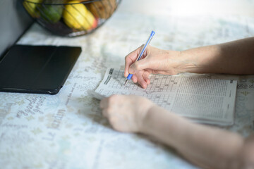 Senior Woman Solving Crossword Puzzle with Tablet and Fruit Bowl in Background