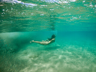 Naklejka premium Underwater view of a woman swimming with a school of fish in Fernando de Noronha, Brazil