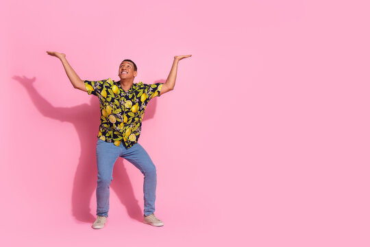Full size photo of pretty young male look up hold ceiling empty space wear trendy tropical print outfit isolated on pink color background