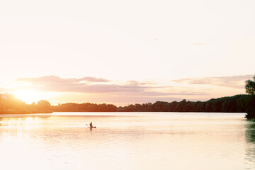 Fototapeta premium canoeing life style hobby activity concept of swimming person on a water in warm sunset light horizon background with landscape trees silhouettes