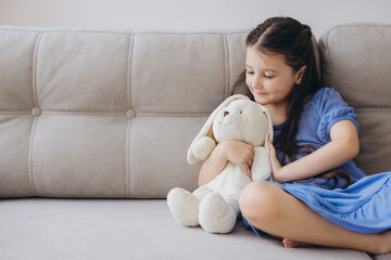 Little Girl Cuddling Plush Bunny on Sofa at Home