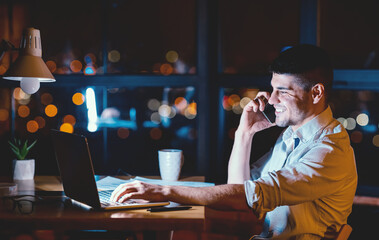 Male Entrepreneur Talking On Cellphone Working On Laptop Overnight In Modern Office. Business Lifestyle. Copy Space