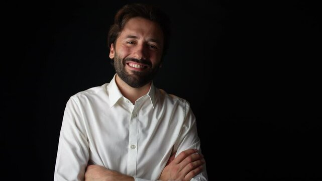 A young Caucasian man in a white shirt smiles at the camera while confidently crossing his arms