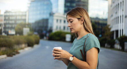 Beautiful Caucasian woman in green blazer going to work with coffee walking near office building.