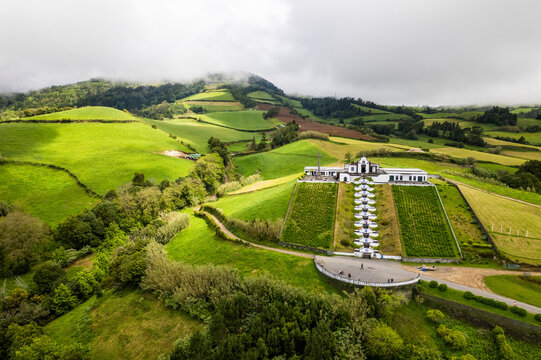 Aerial view of the beautiful Ermida de Nossa Senhora da Paz church surrounded by lush green fields and hills, Vila Franca do Campo, Portugal.