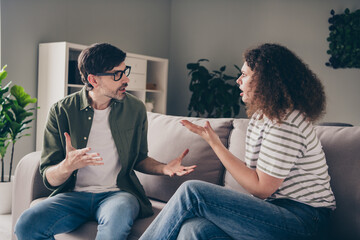Portrait of two young partners sit sofa talk complain living room flat indoors