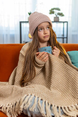 Sick ill girl child wrapped in blanket shivering from cold drinking hot herbal medical tea in...