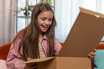 Happy amazed young child kid girl unpacking delivery parcel. Surprised satisfied teen shopper, online shop customer opening cardboard box receiving purchase gift by fast postal shipping at home.