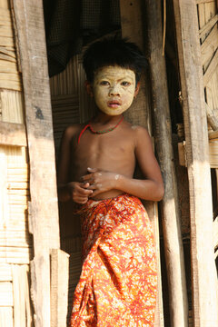Bangladeshi tribal child standing on the doorway of his house with face makeup 