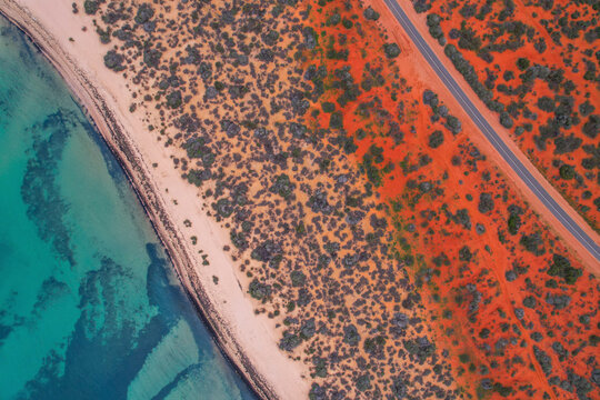 Aerial view of beautiful turquoise ocean and serene beach with red earth and remote road, Monkey Mia, Shark Bay, Gascoyne Region, Australia.