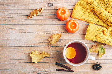 Autumn aesthetic concept. Cup of tea, candles, autumn leaves and yellow sweater on wooden background. Top view, flat lay, copy space