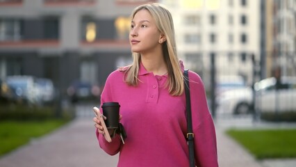 A stylish and fashionable young woman happily enjoys her coffee while strolling through a vibrant modern urban area