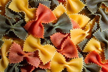 Uncooked Vibrant Colored Farfalle Pasta: A Culinary Canvas of Multicolored Bow-Tie Macaroni, Creating a Lively and Textured Background for Gourmet Cooking Enthusiasts. Colored Dry Pasta. Raw Macaroni