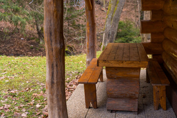 Naklejka premium Rustic wooden table with two benches near a log cabin on a cloudy winter snowless day in a forest.