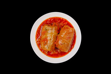 Two cabbage rolls stuffed with minced meat in vegetable gravy on a white platter isolated on black background top view