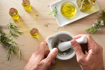 Person preparing rosemary oil essences with mortar on wooden table