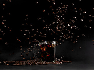 Ice americano Coffee in glass with roasted bean falling. Black background isolated element. Many Coffee Beans fall on Ice cold drink with aroma scent