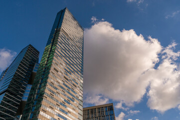 Obraz premium Angled view of modern skyscrapers in business district against blue sky. Looking Up high-rise office buildings. Evening time, sunset. Orange, yellow and gold shades of color.