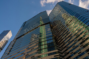 Naklejka premium Angled view of modern skyscrapers in business district against blue sky. Looking Up high-rise office buildings. Evening time, sunset. Orange, yellow and gold shades of color.