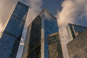 Obraz premium Angled view of modern skyscrapers in business district against blue sky. Looking Up high-rise office buildings. Evening time, sunset. Orange, yellow and gold shades of color.