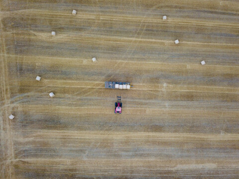 Aerial view of agricultural field with tractor and hay bales in the countryside, Pyecombe, United Kingdom.