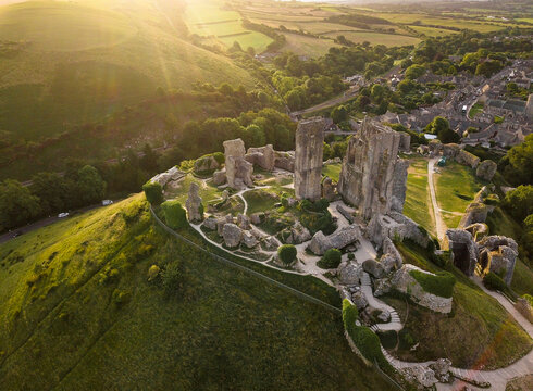 Aerial view of the historic ruins of Corfe Castle surrounded by a scenic countryside village and green hills at sunset, Corfe Castle, England.