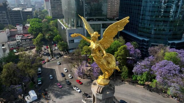 Aerial view of vibrant cityscape featuring the majestic angel statue surrounded by jacaranda trees and bustling traffic, Cuauhtemoc, Mexico.