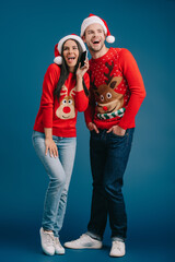 A cheerful couple in playful holiday sweaters shares excitement while celebrating Christmas in a cozy setting.