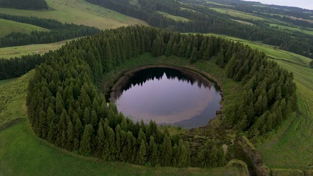 Aerial view of serene and picturesque Lagoa Pau Pique surrounded by lush forest and trees, Capelas, Portugal.