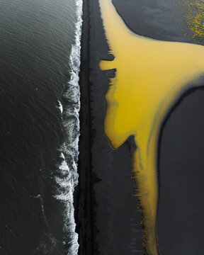 Aerial view of vibrant yellow waves meeting the serene shore, Highlands, Iceland.