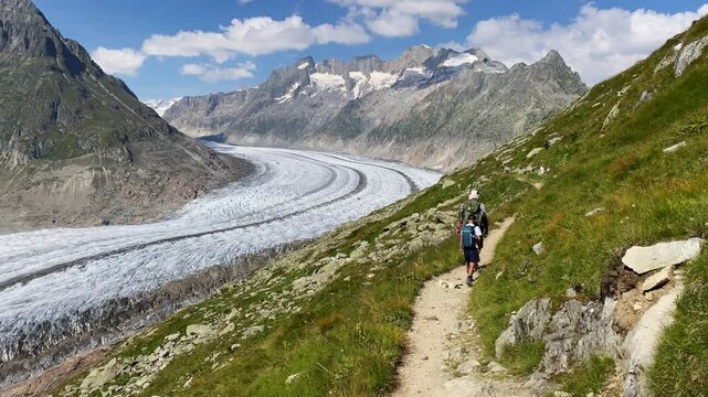 Father and son hiking on trail along majestic Aletsch glacier in Swiss alps
