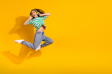 Obraz premium Full size photo of pretty young girl jump touch headphones wear striped t-shirt isolated on yellow color background