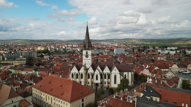 Stunning aerial view of the historic Church of the Holy Trinity in Sibiu, Romania, with its iconic clock tower and tiled roof. Catedrala Evanghelică "Sf&acirc;nta Maria"