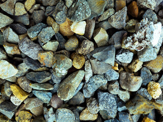 The photo shows a close-up of a collection of small, irregularly shaped rocks. The rocks are of various sizes and colors, including shades of gray, brown, and yellow. 