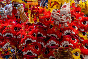 Fototapeta premium A close up shot of multiple red dragon masks with fur and decorative details. Colorful plastic toys and paper lanterns in the background