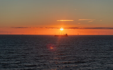 Silhouette of  a transport ship close to the sun. Wind farm in the background, North Sea during sunset, Netherlands.