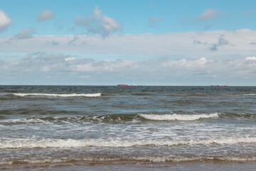 Waves at the beach, transport ships and offshore wind farm in the background.