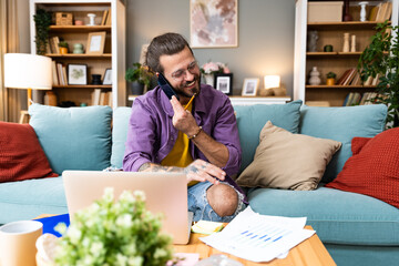 Young professional business man working at home with laptop and papers on desk. Happy freelancer expatriate in home office work on computer communicating with clients and checking data.