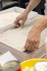 Close-up side view of male cook hands preparing thin rectangular pizza dough on professional kitchen table in pizzeria or italian restaurant. Soft focus. Copy space. Food service business theme.
